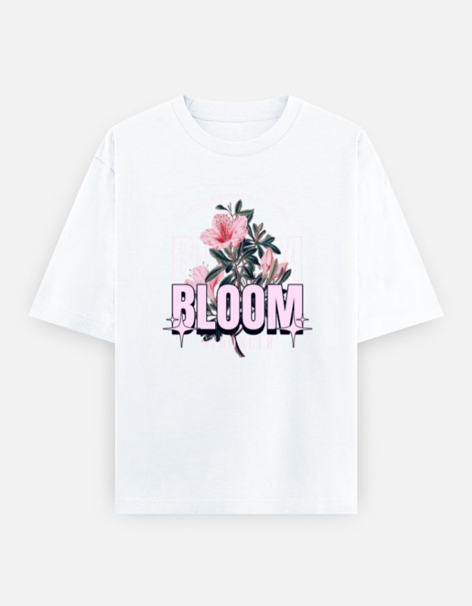 White oversized unisex t shirt featuring a front print with the word BLOOM in bold pastel typography layered with delicate pink flowers and botanical artwork. Made from premium 240 GSM 100% cotton with a relaxed oversized fit. Available in Black and Cream by Shisha.
