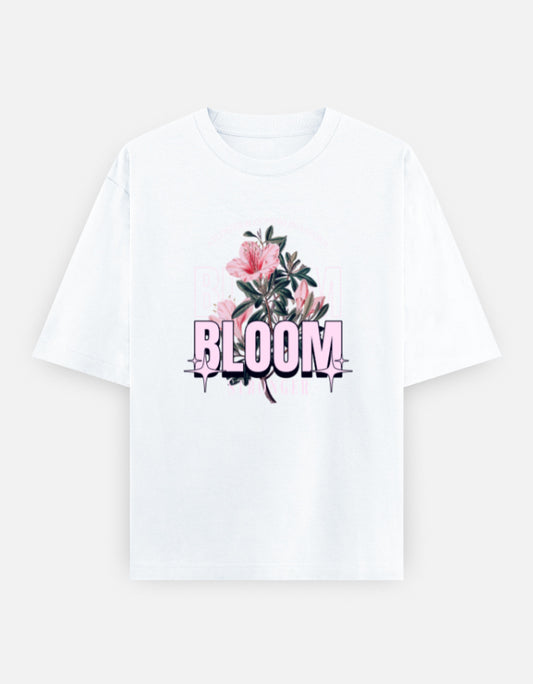 White oversized unisex t shirt featuring a front print with the word BLOOM in bold pastel typography layered with delicate pink flowers and botanical artwork. Made from premium 240 GSM 100% cotton with a relaxed oversized fit. Available in Black and Cream by Shisha.