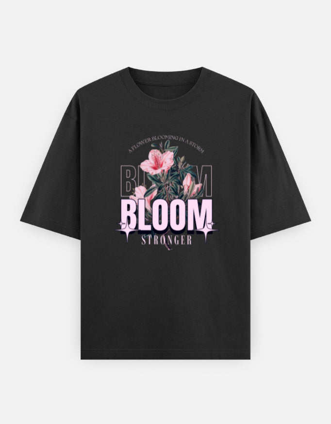 Black oversized unisex t shirt featuring a front print with the word BLOOM in bold pastel typography layered with delicate pink flowers and botanical artwork. Made from premium 240 GSM 100% cotton with a relaxed oversized fit. Available in Black and Cream by Shisha.