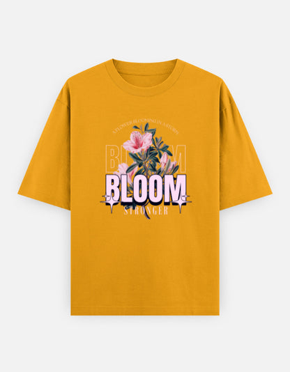 Yellow oversized unisex t shirt featuring a front print with the word BLOOM in bold pastel typography layered with delicate pink flowers and botanical artwork. Made from premium 240 GSM 100% cotton with a relaxed oversized fit. Available in Black and Cream by Shisha.