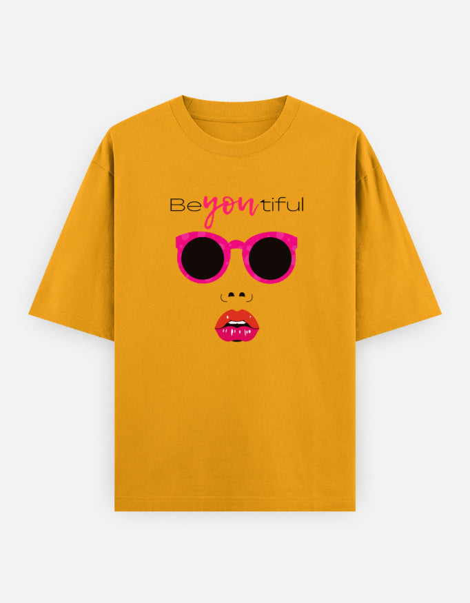 yellow oversized unisex t shirt featuring a front print of a minimalist fashion face with bright pink sunglasses, bold pink lips, and the word Beyoutiful above.