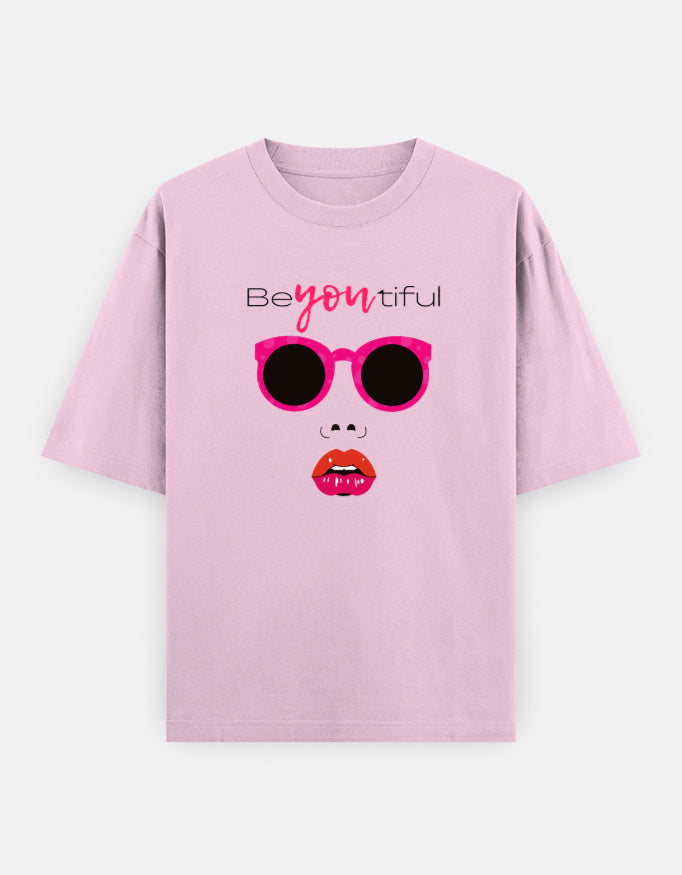 Pink oversized unisex t shirt featuring a front print of a minimalist fashion face with bright pink sunglasses, bold pink lips, and the word Beyoutiful above.