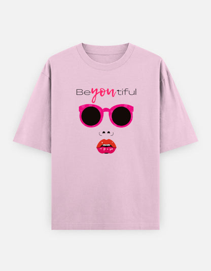 Pink oversized unisex t shirt featuring a front print of a minimalist fashion face with bright pink sunglasses, bold pink lips, and the word Beyoutiful above.