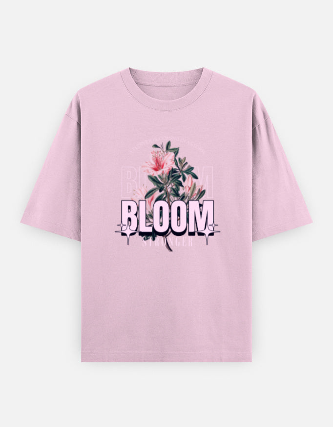Pink oversized unisex t shirt featuring a front print with the word BLOOM in bold pastel typography layered with delicate pink flowers and botanical artwork. Made from premium 240 GSM 100% cotton with a relaxed oversized fit. Available in Black and Cream by Shisha.