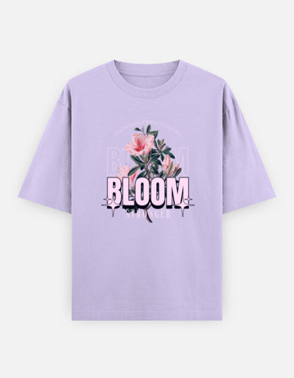 Lavender oversized unisex t shirt featuring a front print with the word BLOOM in bold pastel typography layered with delicate pink flowers and botanical artwork. Made from premium 240 GSM 100% cotton with a relaxed oversized fit. Available in Black and Cream by Shisha.