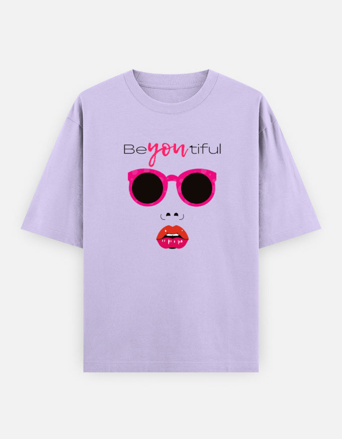 Lavender oversized unisex t shirt featuring a front print of a minimalist fashion face with bright pink sunglasses, bold pink lips, and the word Beyoutiful above.