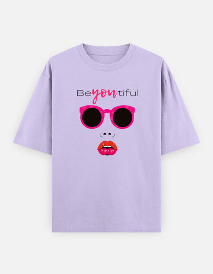Lavender oversized unisex t shirt featuring a front print of a minimalist fashion face with bright pink sunglasses, bold pink lips, and the word Beyoutiful above.