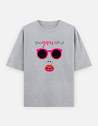 grey oversized unisex t shirt featuring a front print of a minimalist fashion face with bright pink sunglasses, bold pink lips, and the word Beyoutiful above.