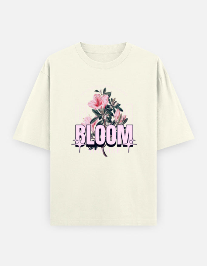 Off-White oversized unisex t shirt featuring a front print with the word BLOOM in bold pastel typography layered with delicate pink flowers and botanical artwork. Made from premium 240 GSM 100% cotton with a relaxed oversized fit. Available in Black and Cream by Shisha.