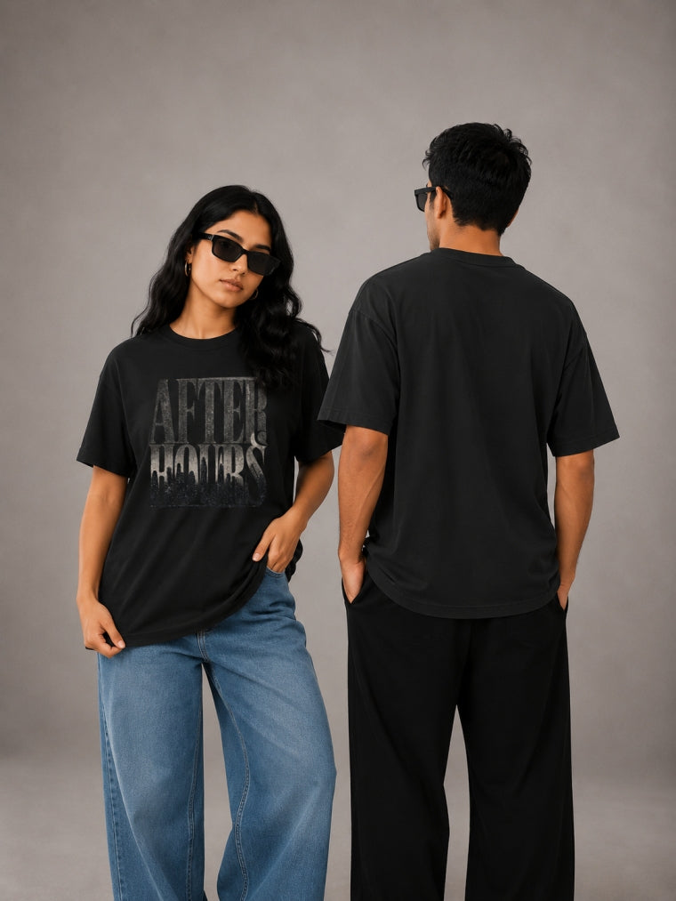 Two people wearing black t-shirts with text, one facing the camera and the other with back to the camera, on a gray background.
