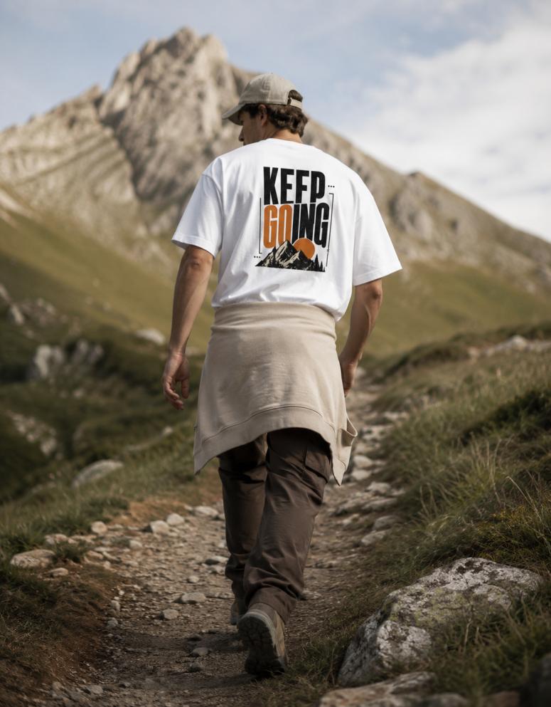 Person hiking on a mountain path wearing a t-shirt with 'Keep Going' text.